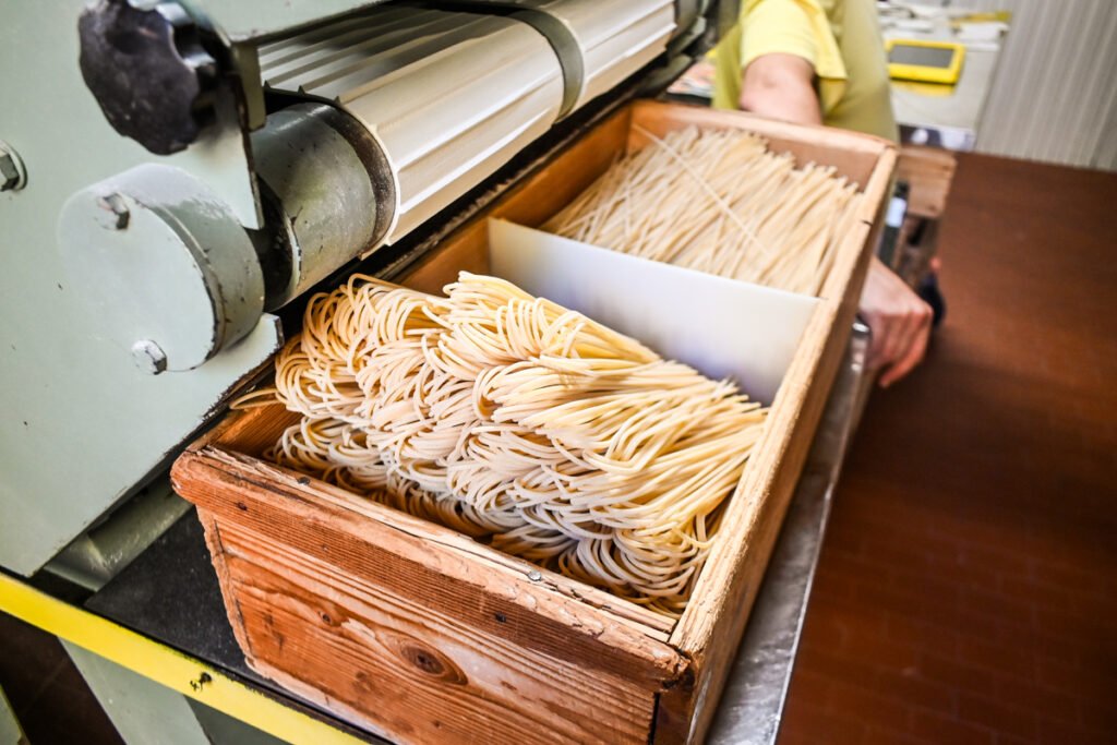 Handgemachte Spaghetti in einer Holzschachtel, frisch von der Nudelmaschine. Traditionelle italienische Pasta in Frankfurt, hergestellt mit hochwertigen Zutaten für authentischen Geschmack.