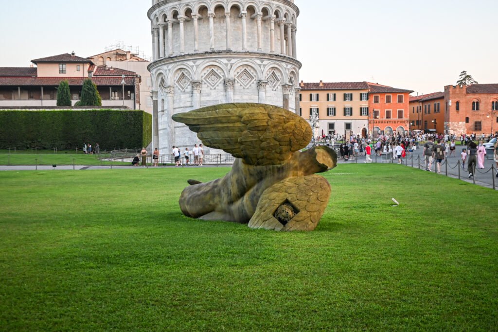 Verlorener Engel Skulptur vor dem Schiefen Turm von Pisa, touristische Sehenswürdigkeit in Pisa, Italien, lokaler Kunst- und Kulturschauplatz, historische Architektur und kreative Gartengestaltung.